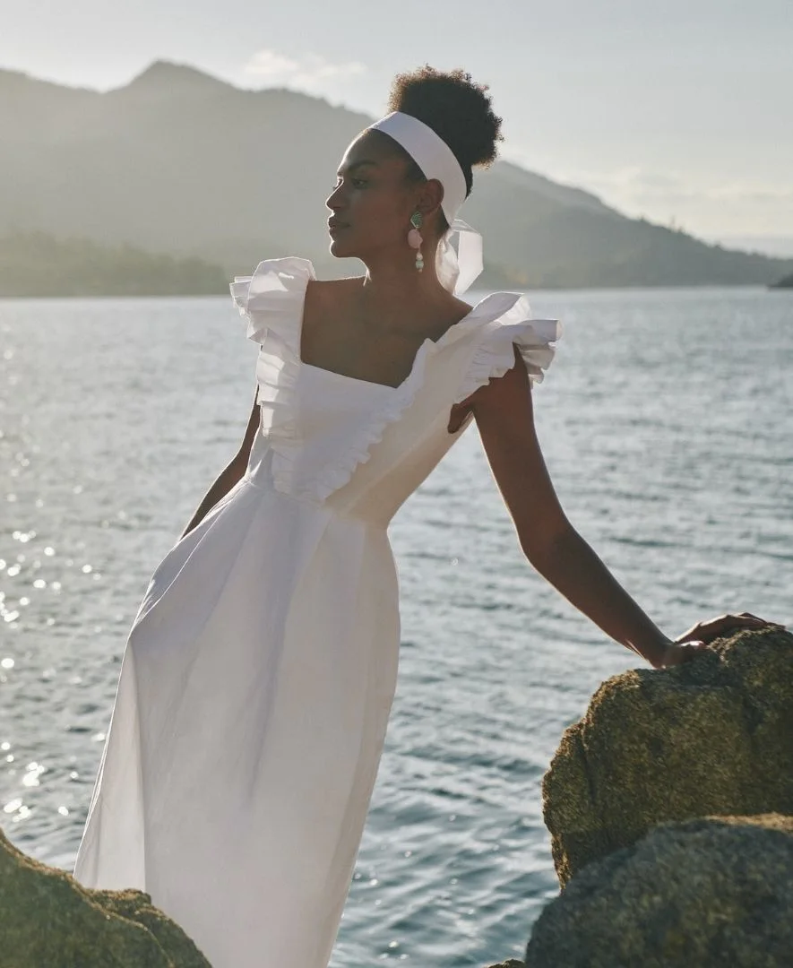 Woman wearing a white ruffled TROUT dress beside a mountain lake